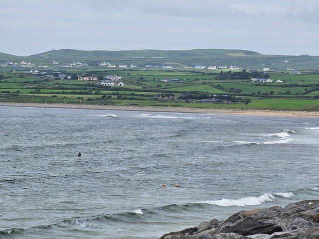 solid lines of swell along the beach with a few dippers and anoverly optomistic surfer in the water at high tide